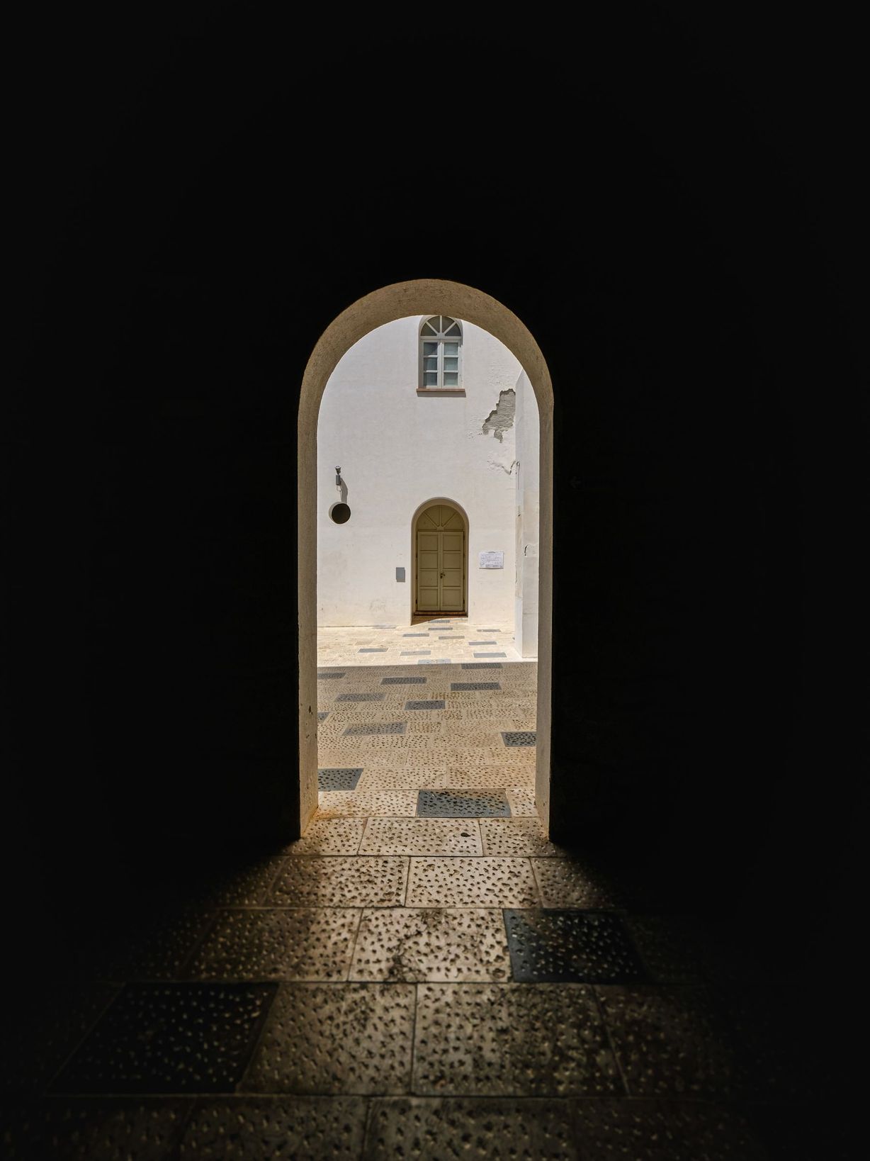 A thick stone arch opening onto a sunlit whitewashed courtyard